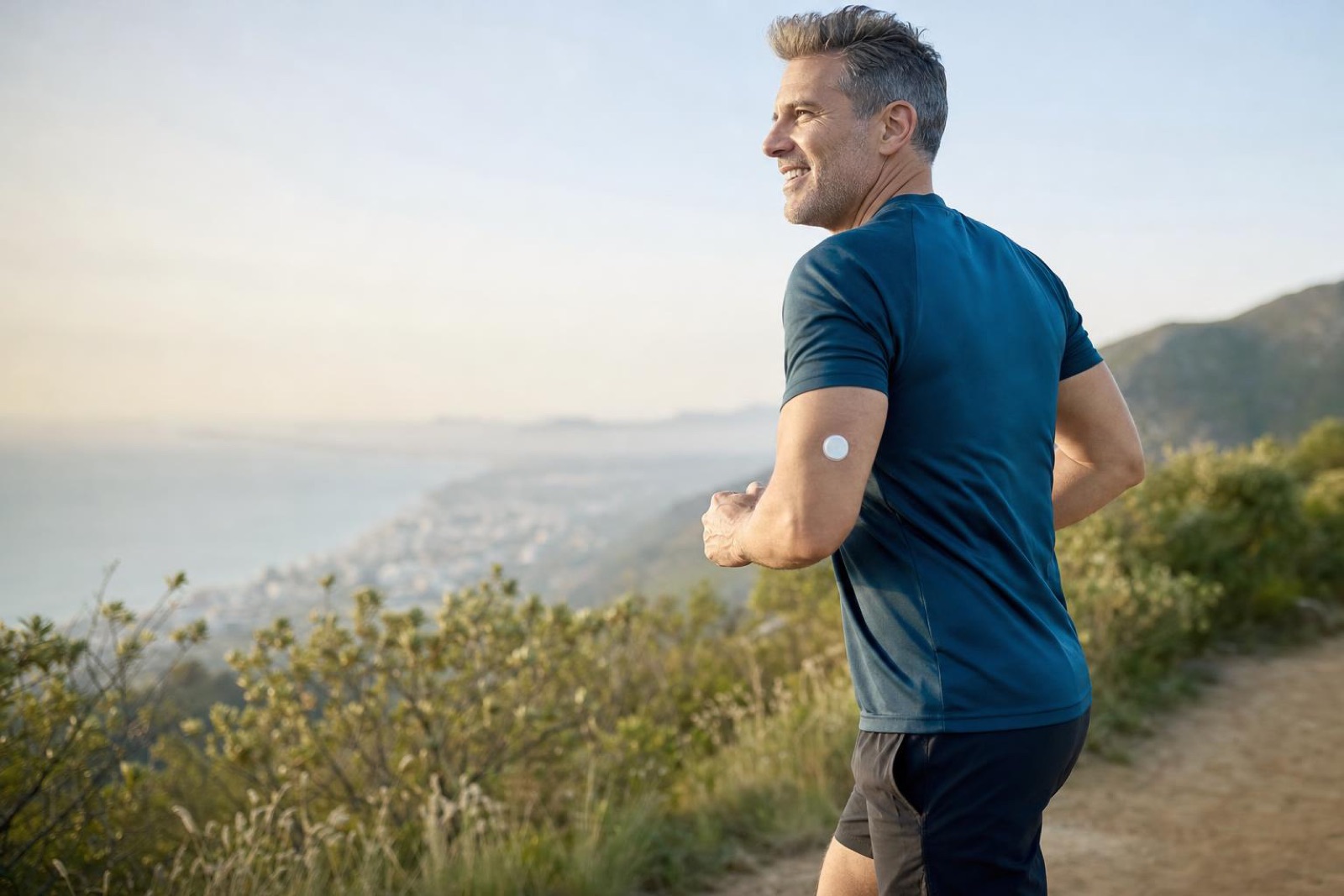 Man in his 40s running a coastal trail wearing a glucose monitor sensor on his arm